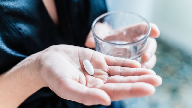 Mulher segura comprimido anti-histamínico numa mão e um copo com água na outra mão.