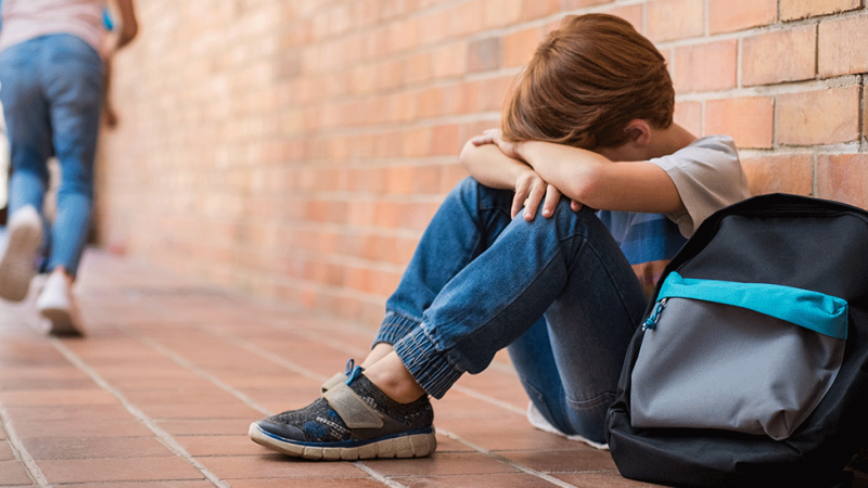 Criança vítima de bullying sentada no chão a chorar