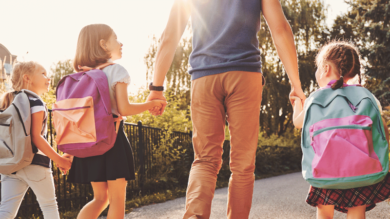 Pai acompanha os filhos e assegura-se de que estão a usar corretamente a mochila