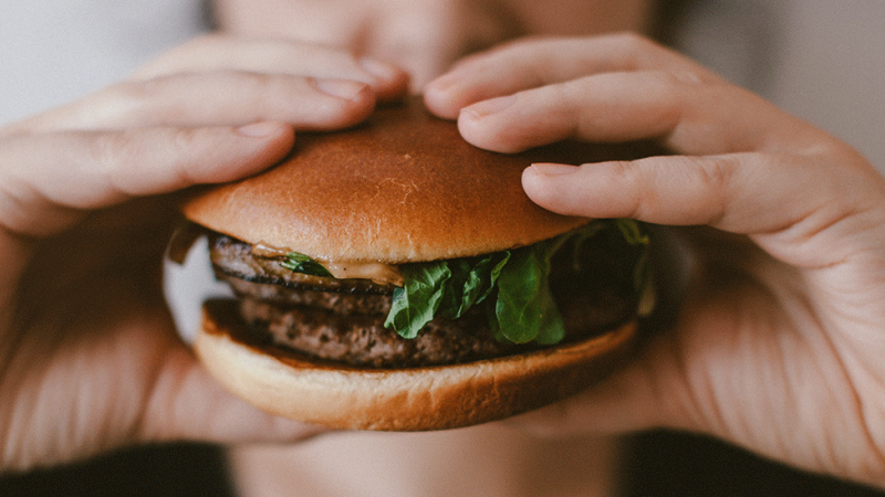 Pessoa stressada come hambúrguer demonstrando que o stress engorda