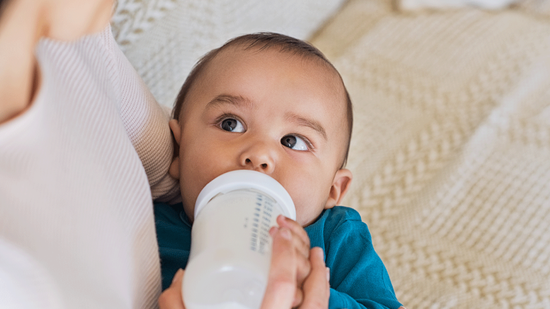 Mãe dá o biberão ao seu filho, seguindo regras de alimentação do bebé