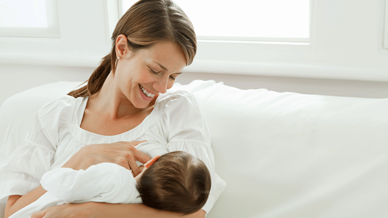 Mãe sentada no sofá com o seu bebé ao colo durante amamentação