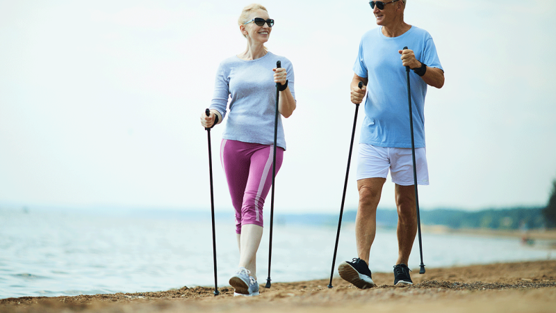 Homem e mulher caminham com bastões para prevenir lesões
