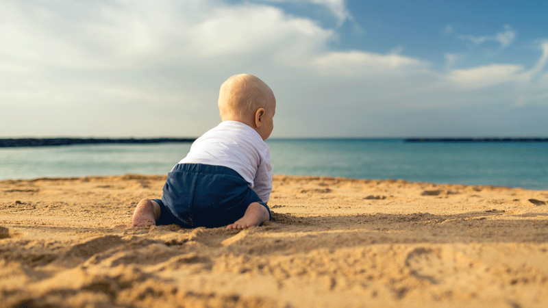 Bebé brinca na areia com roupa fresca, um dos cuidados a ter com bebés na praia