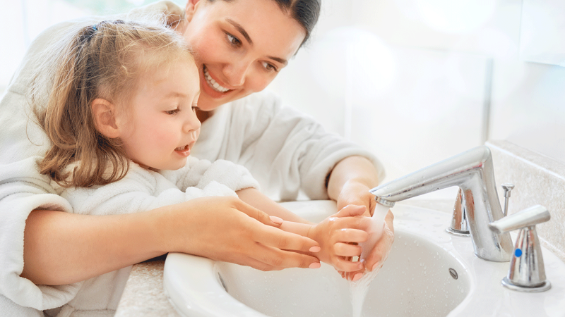Mãe ensina filha a lavar as mãos para proteger-se de gripes e constipações