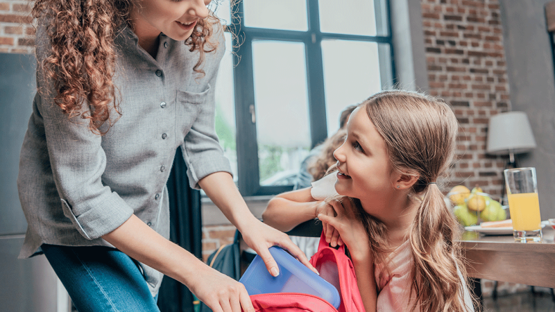 Mãe ajuda filha a preparar lancheira no regresso às aulas