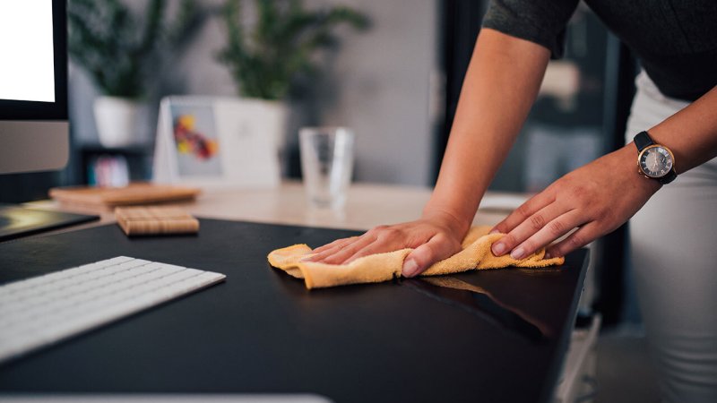Mulher desinfecta secretária do trabalho para prevenir infeção por COVID-19