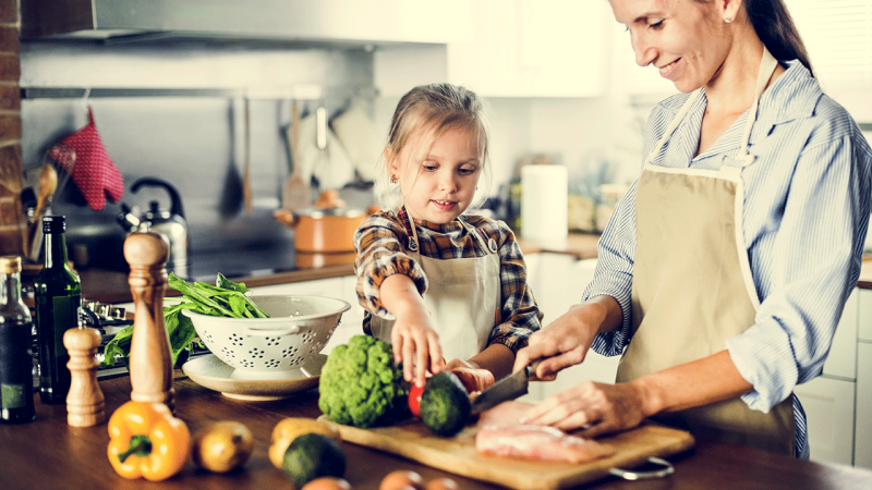 Filha ajuda mãe a preparar refeição como incentivo para comer fruta e verduras
