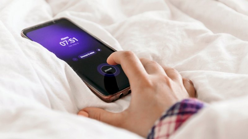 pessoa a tocar no botão snooze do telemóvel