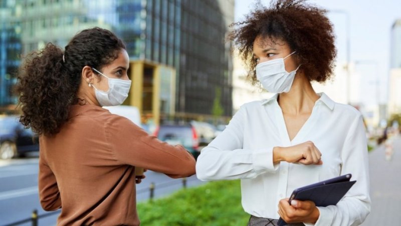 pessoas a cumprimentarem-se com os cotovelos e usando máscaras