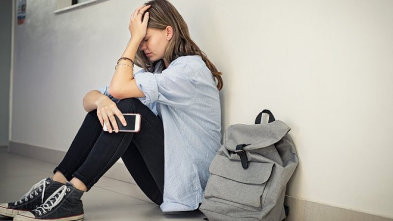 jovem sentada no chão triste com telemóvel na mão