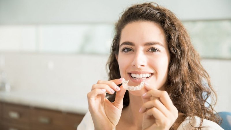Mulher jovem no dentista coloca alinhadores dentários invisíveis