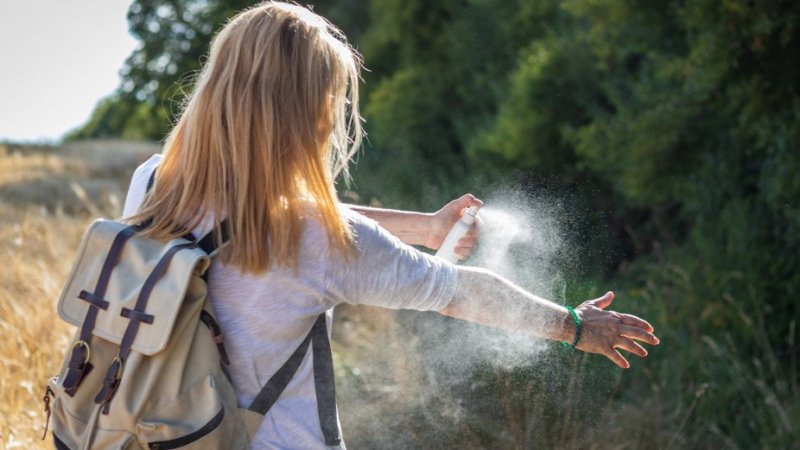 mulher a aplicar spray contra mosquitos para evitar febre da carraça.