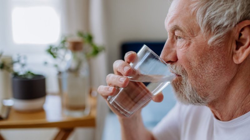 Homem idoso bebe água para se proteger do calor