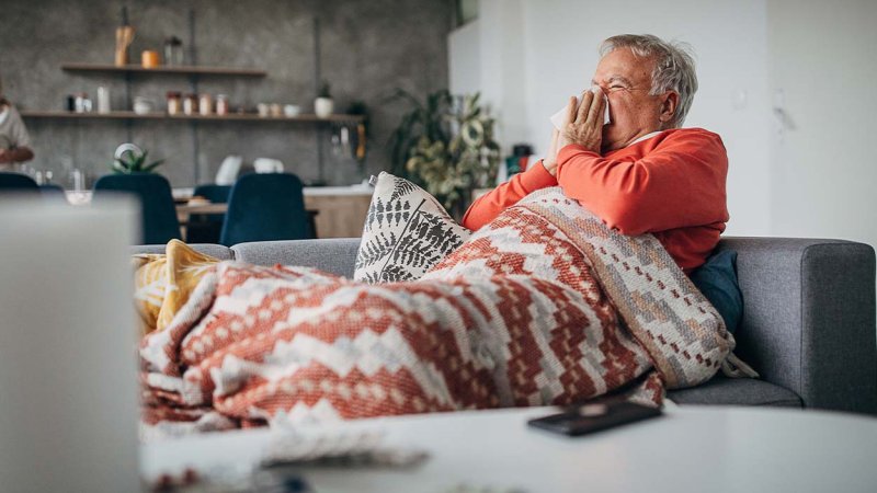 Homem sentado no sofá com sintomas de gripe