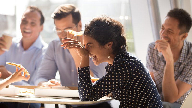 grupo de pessoas que está sentada à mesa a rir enquanto comem.