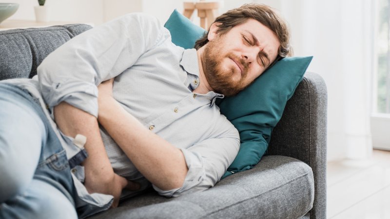 homem  deitado no sofá com expressão de dor com as mãos na barriga devido a Disbiose