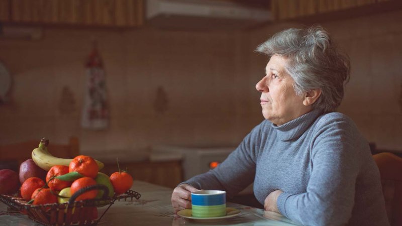 Mulher idosa sozinha, sentada à mesa, apresenta sinais de solidão