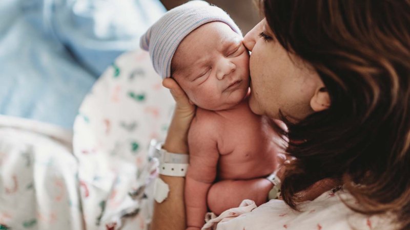 Mãe beija bebé recém-nascido na maternidade