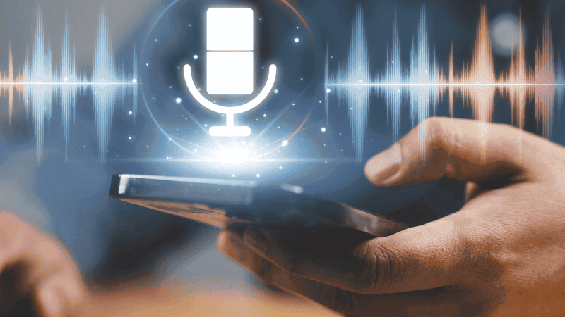 Pessoa a segurar num telemóvel enquanto um ícone digital de microfone e ondas sonoras aparece acima do ecrã, simbolizando tecnologia de gravação ou reconhecimento de voz