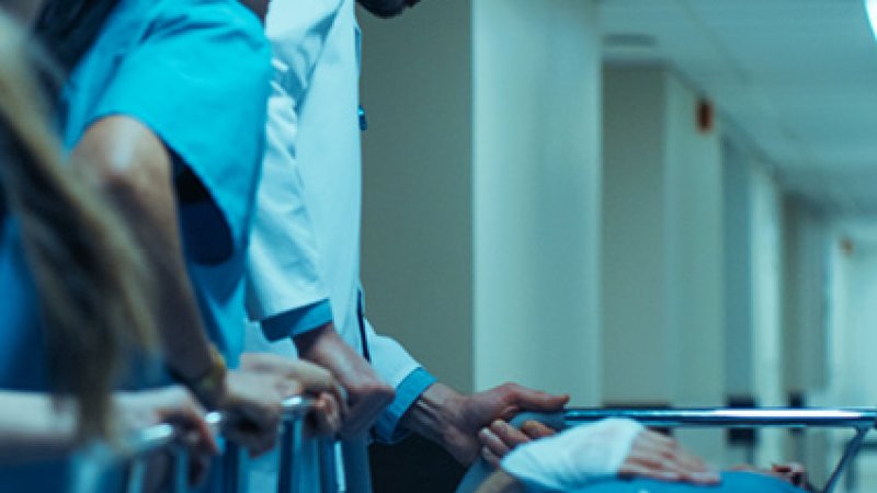 Um médico e duas enfermeiras dão assistência a um paciente deitado numa maca.