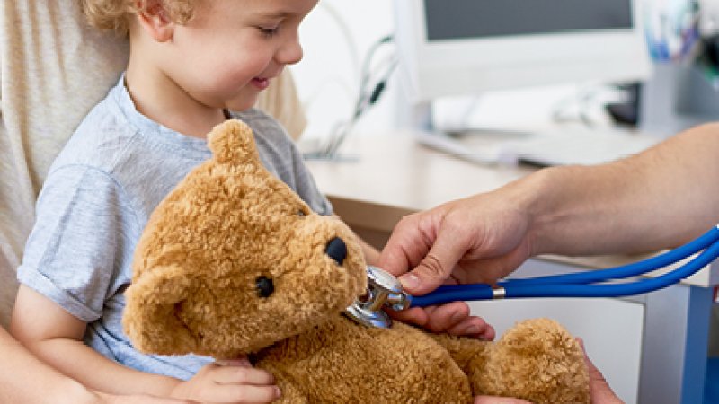 Criança sentada ao colo com um urso de peluche num consultório
