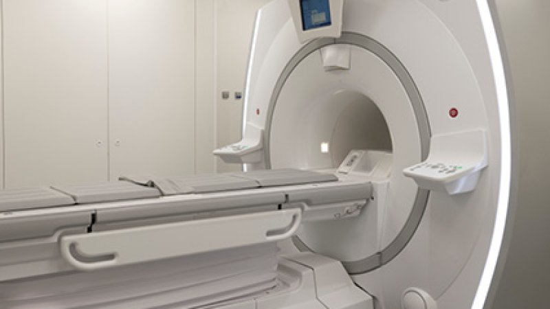 Equipamento moderno de ressonância magnética de grandes dimensões, de cor branca e cinzenta, numa sala hospitalar limpa e iluminada.