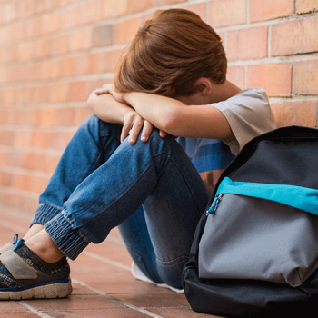 Criança vítima de bullying sentada no chão a chorar