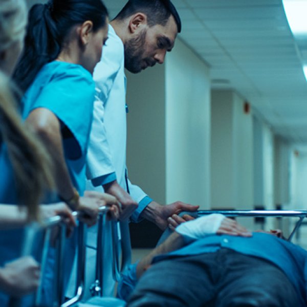 Um médico e duas enfermeiras dão assistência a um paciente deitado numa maca.