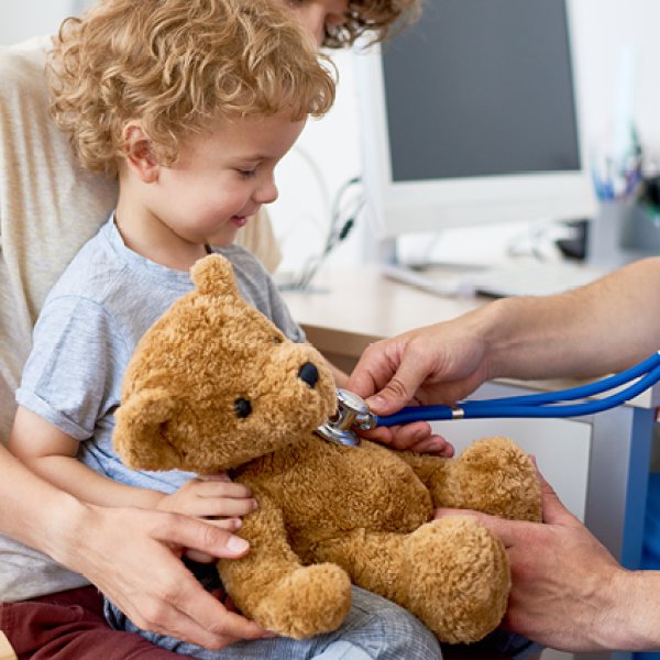 Criança sentada ao colo com um urso de peluche num consultório