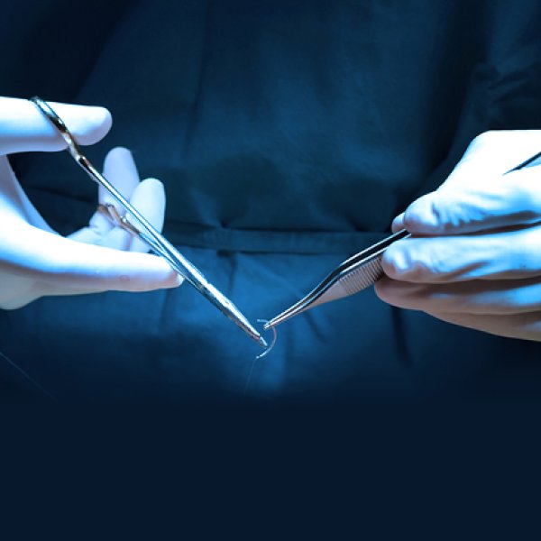 Duas mãos com luvas cirúrgicas manuseando pinças médicas e uma agulha de sutura curvada sob iluminação azulada de centro cirúrgico.