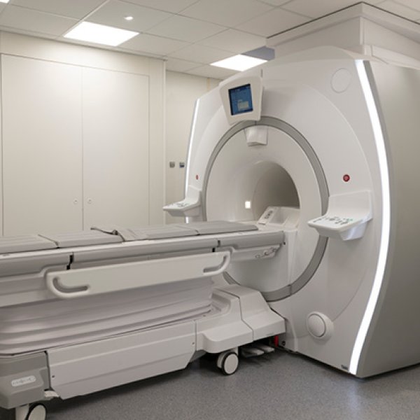 Equipamento moderno de ressonância magnética de grandes dimensões, de cor branca e cinzenta, numa sala hospitalar limpa e iluminada.