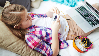 Rapariga na adolescência deitada na cama com aparelhos tecnológicos