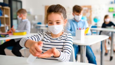 Criança com máscara desinfeta as mãos para se proteger da COVID-19