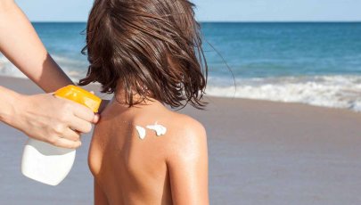 Adulto aplica protetor solar em criança na praia