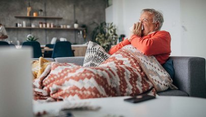 Homem sentado no sofá com sintomas de gripe