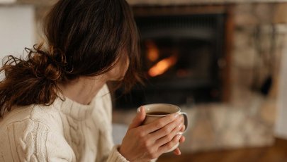 mulher sentada a beber chá em frente a uma lareira para se aquecer