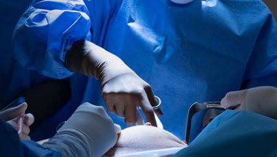 Equipa médica a realizar uma cirurgia, com profissionais de saúde equipados com bata, luvas e máscara e um paciente em ambiente hospitalar.