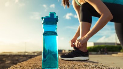 Garrafa de água em grande plano, com mulher a atar uma sapatilha no fundo.