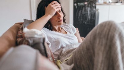 Mulher doente no sofá mete mão na cabeça.